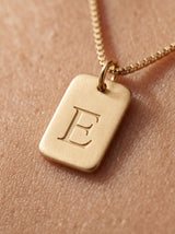 Collar Inicial de Emma Montiel puesto: mujer con camisa de lino y colgante con inicial grabada en acabado dorado cálido.